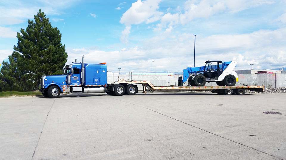 Blue semi truck transporting heavy equipment in the form ofa forklift